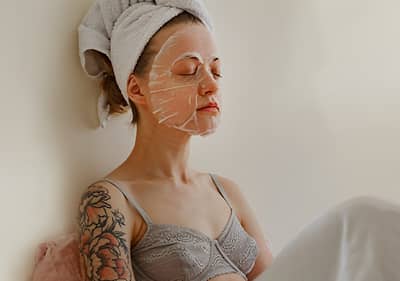 Frau mit Gesichtsmaske und Handtuch auf den Haaren