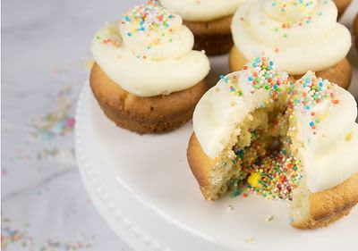 Angeschnittene Cupcakes mit weißem Topping und bunten Zuckerkugeln