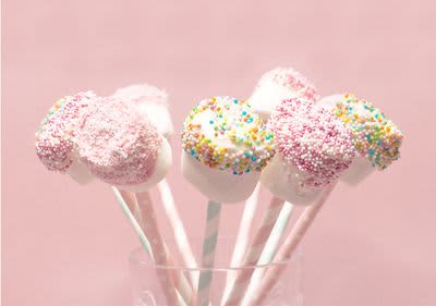 Weiße Marshmallow Pops dekoriert mit bunten Zuckerkugeln auf einem rosanen Hintergrund in einem Glas